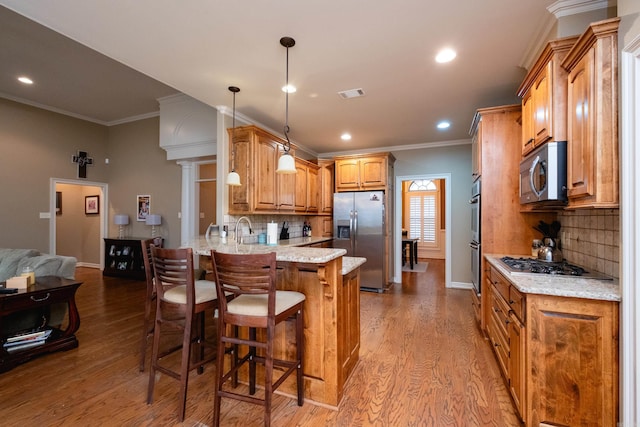 kitchen with appliances with stainless steel finishes, pendant lighting, a breakfast bar area, light stone counters, and light wood-type flooring