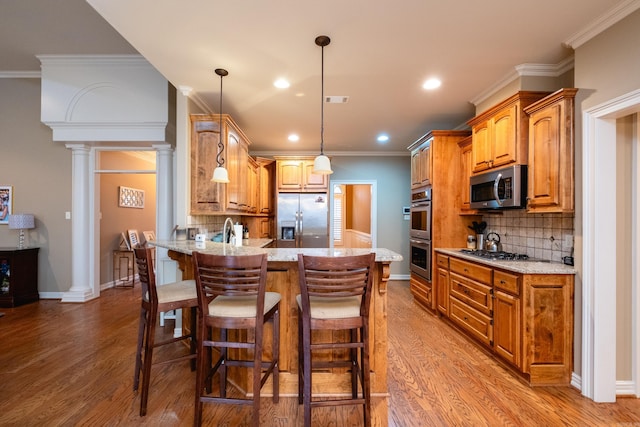 kitchen with appliances with stainless steel finishes, decorative columns, light stone counters, decorative light fixtures, and kitchen peninsula