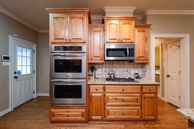 kitchen with appliances with stainless steel finishes, decorative backsplash, ornamental molding, light stone countertops, and light wood-type flooring