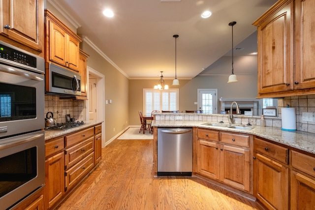 kitchen featuring appliances with stainless steel finishes, sink, hanging light fixtures, light stone counters, and crown molding