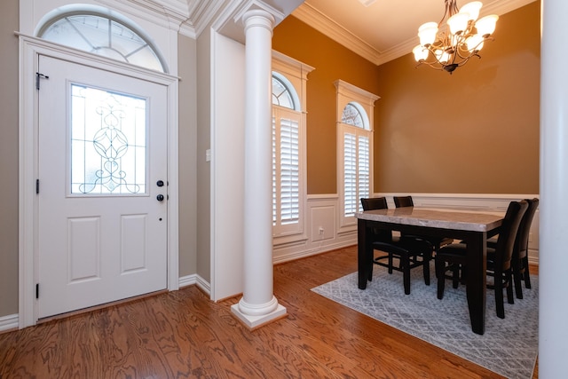 foyer entrance featuring decorative columns, crown molding, hardwood / wood-style flooring, and an inviting chandelier