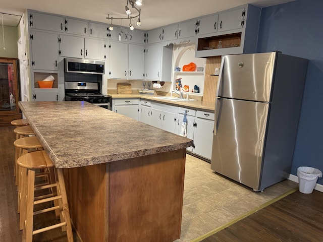 kitchen with a kitchen island, appliances with stainless steel finishes, sink, a breakfast bar area, and light hardwood / wood-style flooring