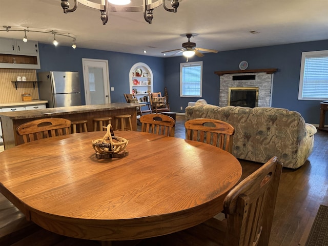 dining area featuring ceiling fan, dark hardwood / wood-style flooring, and a stone fireplace