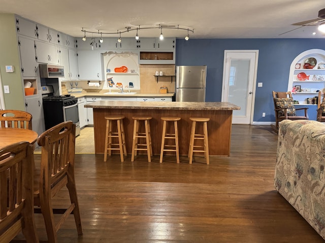 kitchen featuring dark wood-type flooring, a breakfast bar area, ceiling fan, appliances with stainless steel finishes, and a center island