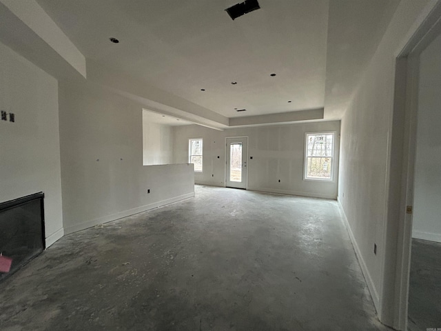 unfurnished living room featuring a healthy amount of sunlight, concrete flooring, and a tray ceiling