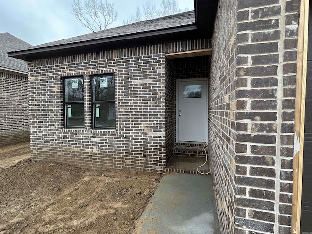 view of exterior entry featuring brick siding and a shingled roof