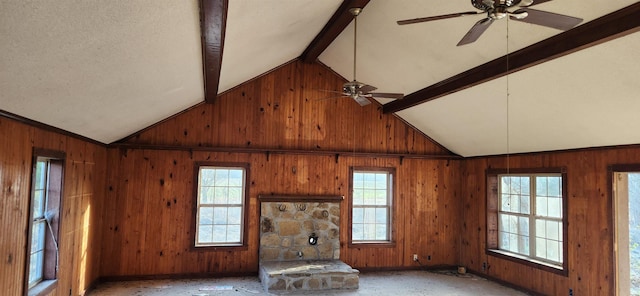 unfurnished living room with a wealth of natural light, lofted ceiling with beams, and wooden walls