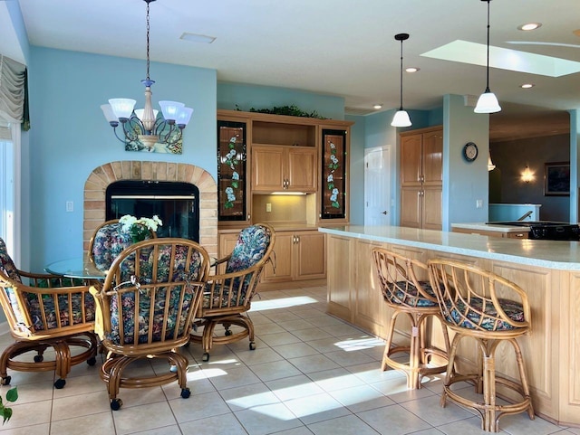 kitchen with light tile patterned flooring, kitchen peninsula, an inviting chandelier, and a brick fireplace