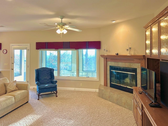 living room featuring a tiled fireplace, light carpet, and ceiling fan