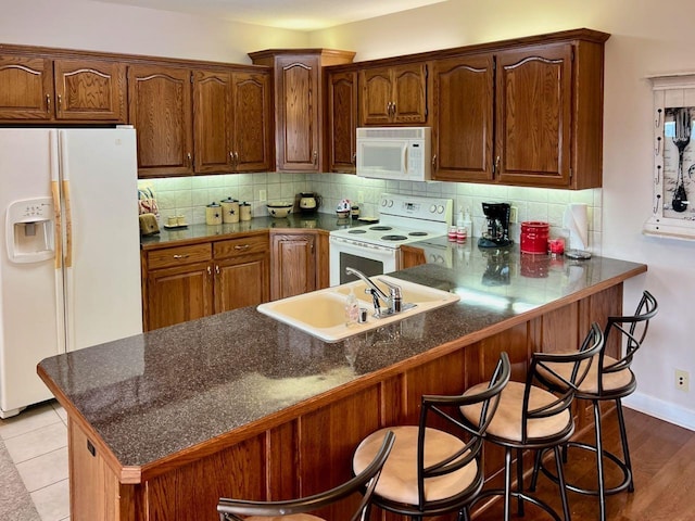 kitchen with white appliances, kitchen peninsula, sink, and a breakfast bar area