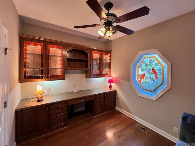 unfurnished office with dark wood-type flooring, ceiling fan, and built in desk