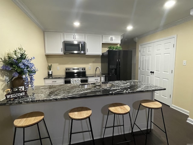 kitchen with sink, appliances with stainless steel finishes, dark stone countertops, a kitchen breakfast bar, and white cabinets