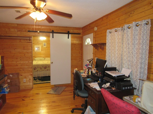 office featuring a barn door, wooden walls, ceiling fan, and light hardwood / wood-style flooring