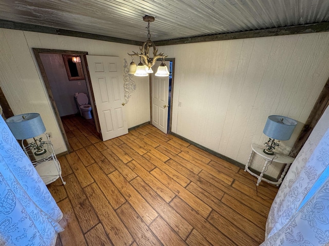 unfurnished dining area with a notable chandelier, wooden walls, wooden ceiling, and light wood-type flooring