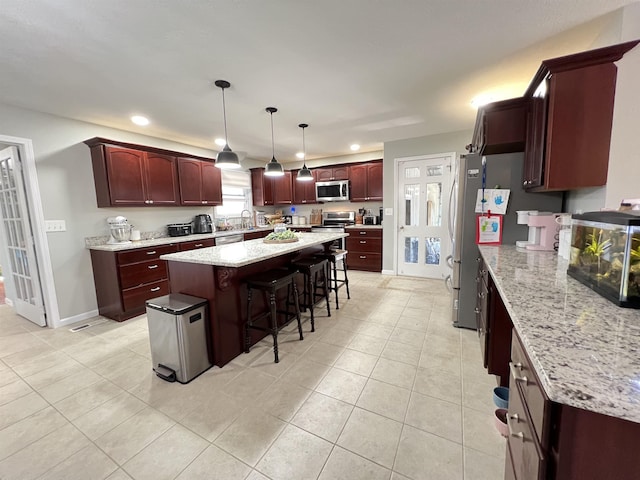 kitchen featuring a breakfast bar area, appliances with stainless steel finishes, hanging light fixtures, a center island, and light stone counters