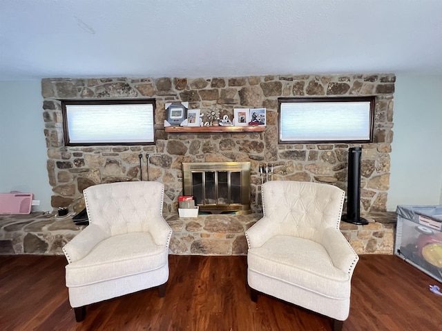 living area featuring a stone fireplace, hardwood / wood-style floors, and a wood stove