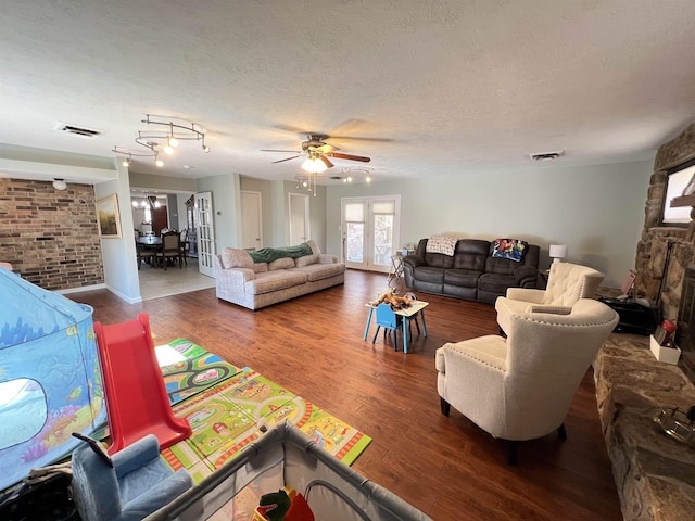 living room featuring wood-type flooring, a stone fireplace, ceiling fan, and a textured ceiling