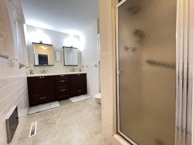 bathroom with a shower with shower door, tile walls, vanity, toilet, and tile patterned floors