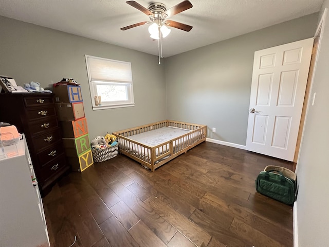 bedroom with dark hardwood / wood-style flooring, a crib, and ceiling fan