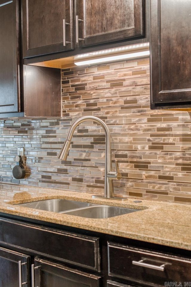 kitchen with tasteful backsplash, dark brown cabinetry, light stone countertops, and sink