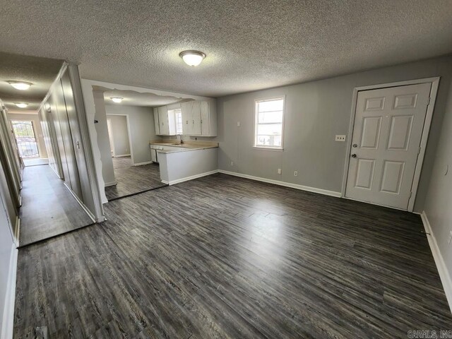 unfurnished living room featuring dark wood-type flooring, a textured ceiling, and baseboards