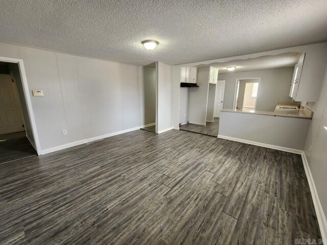 unfurnished living room featuring baseboards, dark wood finished floors, and a textured ceiling