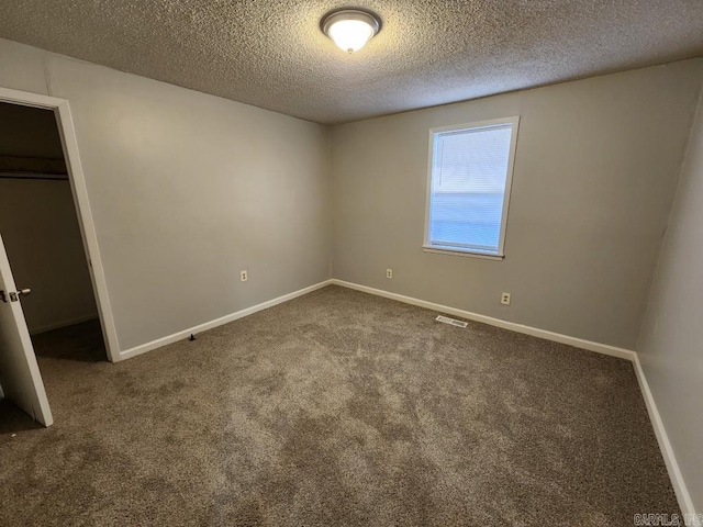 unfurnished bedroom with visible vents, a textured ceiling, dark carpet, and baseboards