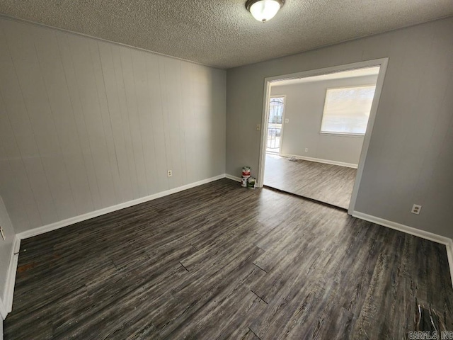 spare room with a textured ceiling, dark wood finished floors, and baseboards