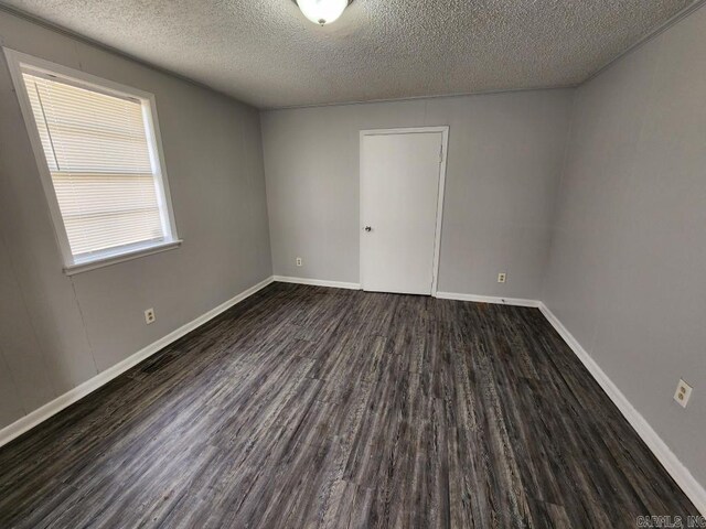 empty room with dark wood-type flooring, a textured ceiling, and baseboards