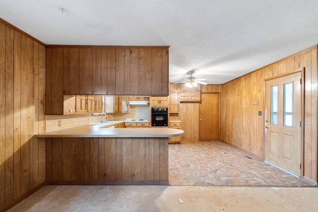 kitchen with kitchen peninsula, wood walls, sink, black appliances, and a textured ceiling