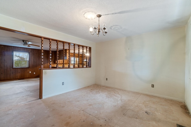 empty room with ceiling fan with notable chandelier, a textured ceiling, and wood walls