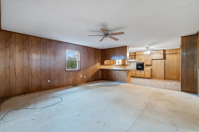 kitchen featuring wooden walls, oven, kitchen peninsula, and ceiling fan