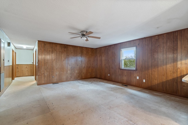 empty room featuring ceiling fan, wooden walls, and a textured ceiling