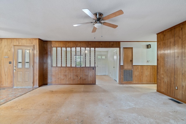 interior space featuring ceiling fan, a textured ceiling, and wooden walls