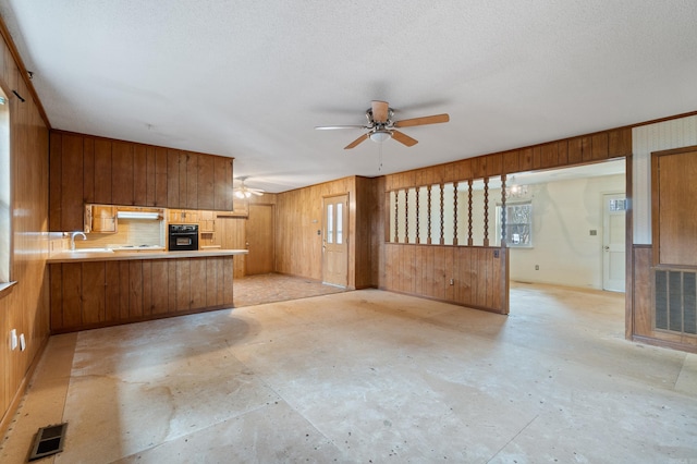 kitchen with sink, wooden walls, kitchen peninsula, black oven, and ceiling fan