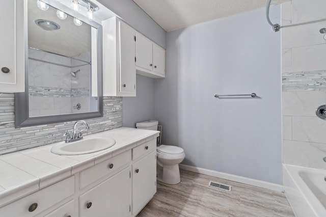 full bathroom featuring tiled shower / bath, hardwood / wood-style floors, tasteful backsplash, vanity, and toilet