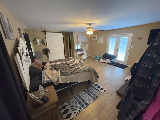 bedroom featuring wood-type flooring, access to outside, ceiling fan, a barn door, and french doors