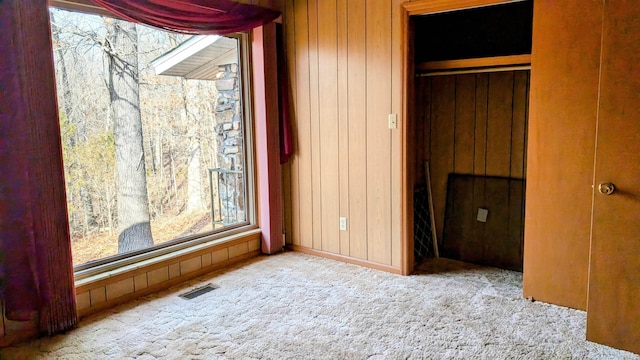 unfurnished bedroom featuring wood walls, a closet, and light colored carpet