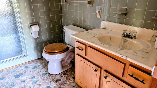 bathroom with tile walls, toilet, vanity, and a shower with shower door