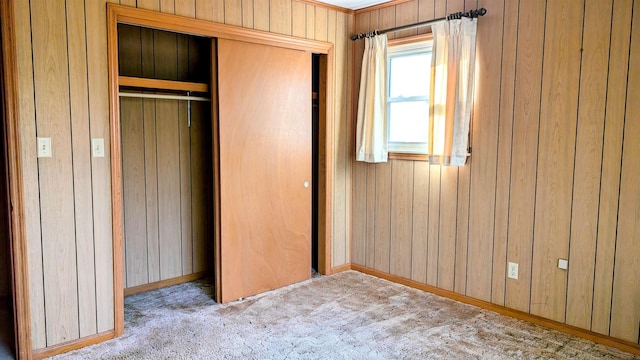 unfurnished bedroom with wood walls, light carpet, and a closet