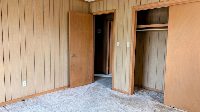 unfurnished bedroom featuring light carpet, a closet, and wooden walls