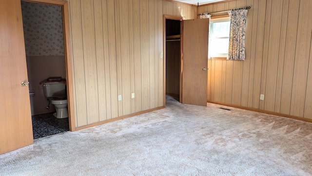 unfurnished bedroom with wood walls, ensuite bath, and light carpet