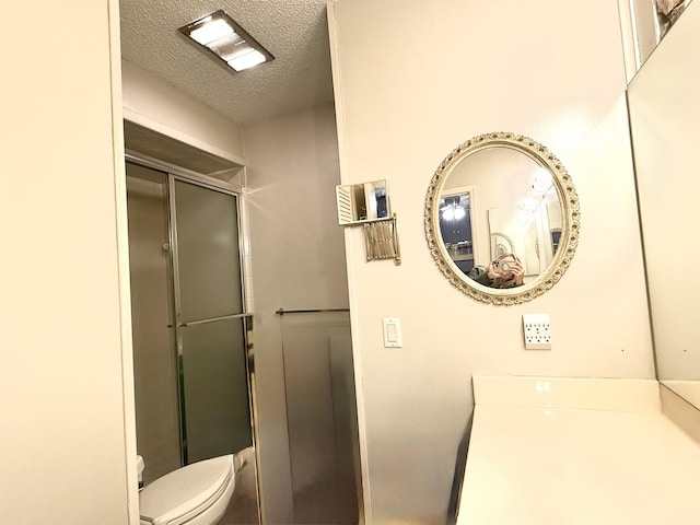 bathroom with vanity, a shower with shower door, toilet, and a textured ceiling