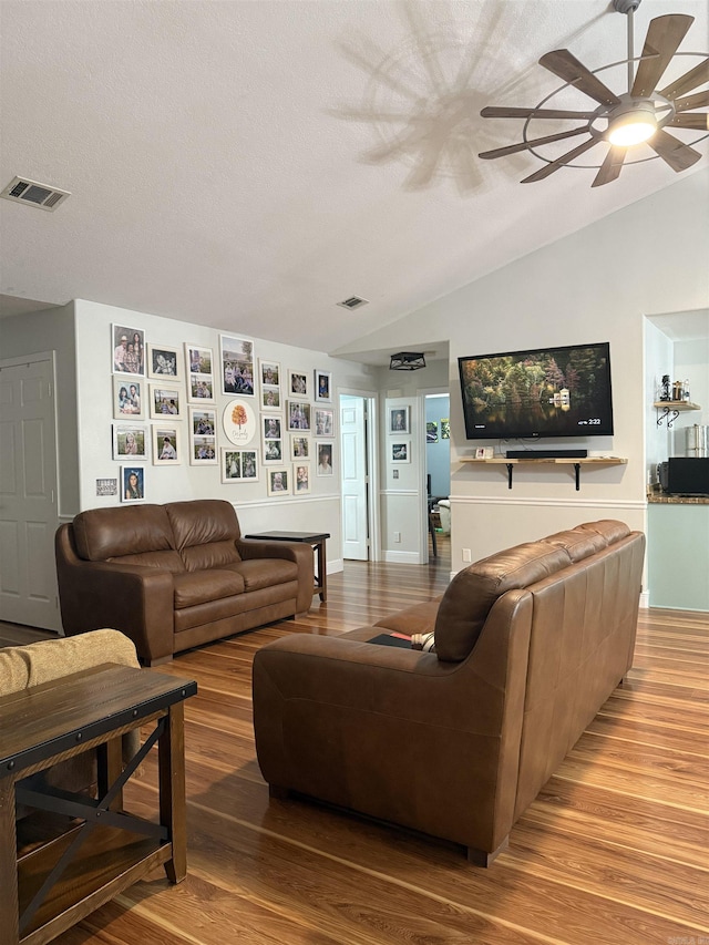 living room with ceiling fan, light hardwood / wood-style flooring, a textured ceiling, and vaulted ceiling