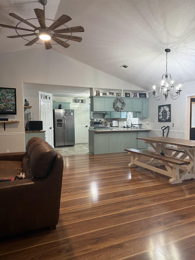 living room with vaulted ceiling, dark hardwood / wood-style floors, ceiling fan with notable chandelier, sink, and a textured ceiling