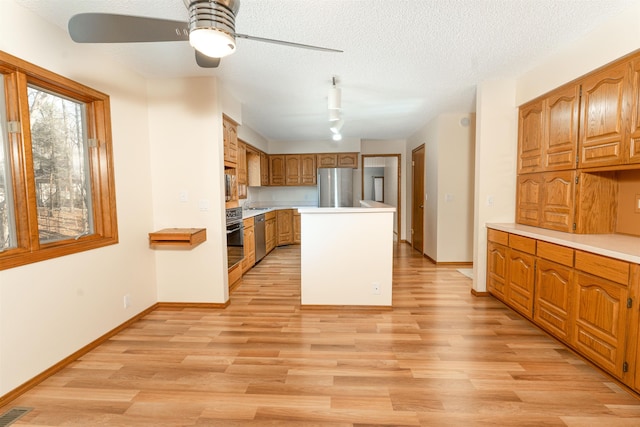 kitchen with light hardwood / wood-style flooring, ceiling fan, stainless steel appliances, a center island, and a textured ceiling