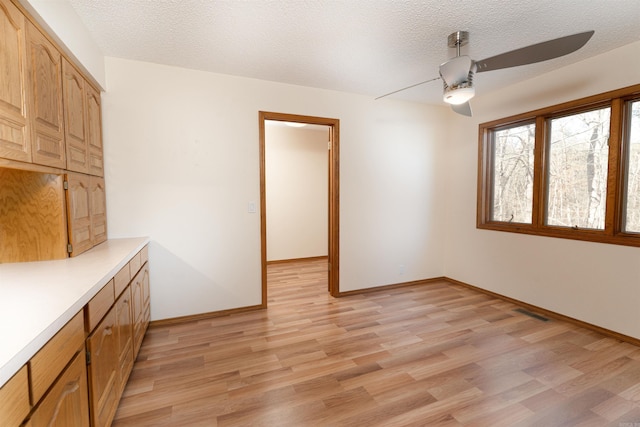 unfurnished dining area with ceiling fan, light hardwood / wood-style floors, and a textured ceiling