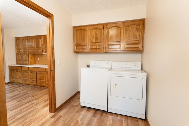 laundry room with cabinets, washing machine and clothes dryer, light hardwood / wood-style floors, and a textured ceiling