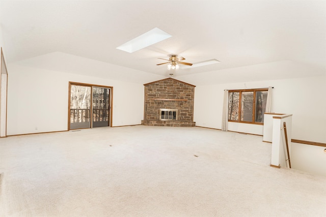 unfurnished living room with ceiling fan, light colored carpet, vaulted ceiling with skylight, and a brick fireplace