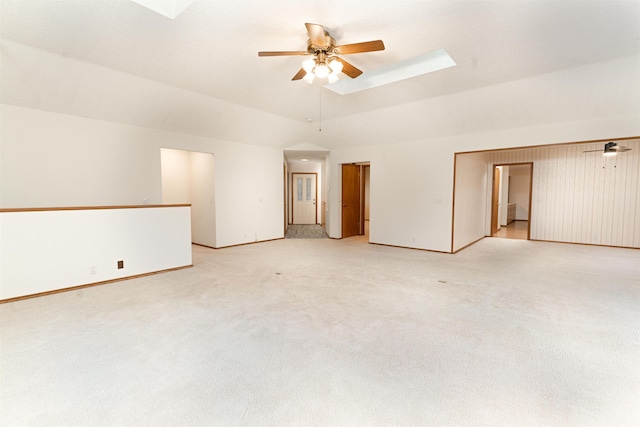 empty room featuring vaulted ceiling with skylight, light colored carpet, a raised ceiling, and ceiling fan